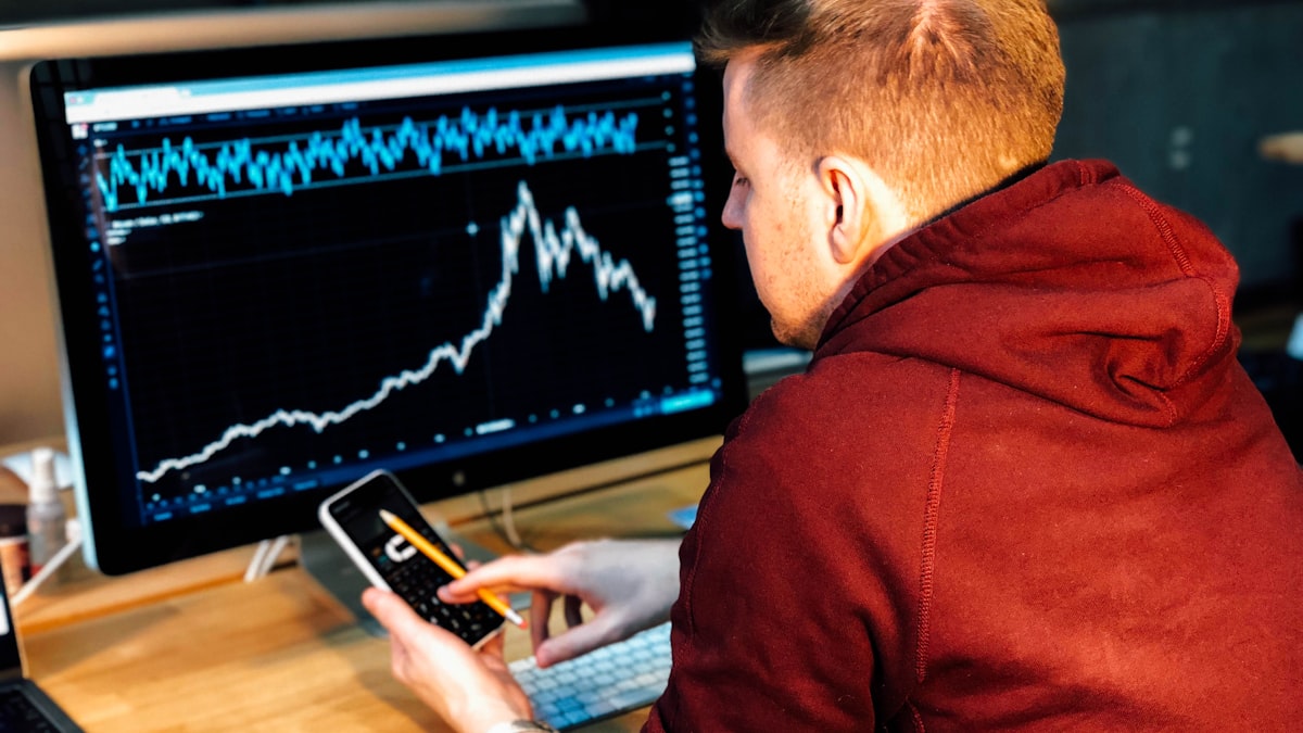 3 Characteristics of Losing Traders – Spotting your Bad Habits — man holding black smartphone with flat screen monitor in front