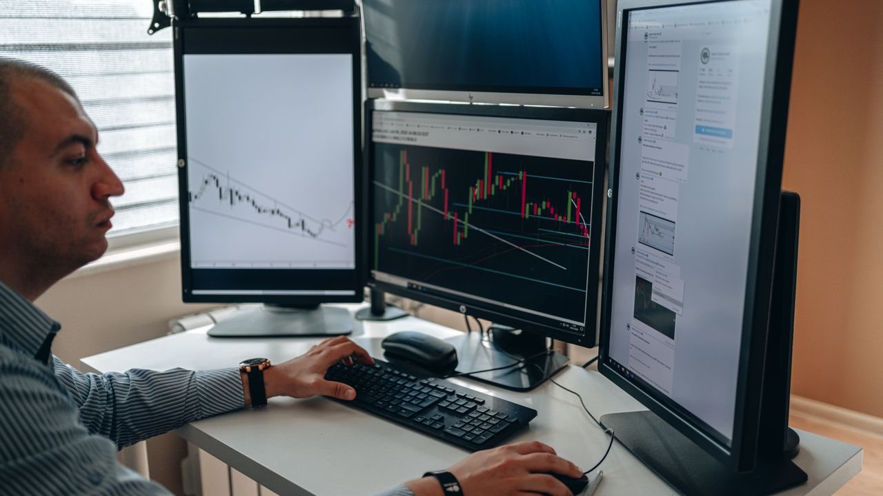 Man at a desk with several monitors showing charts