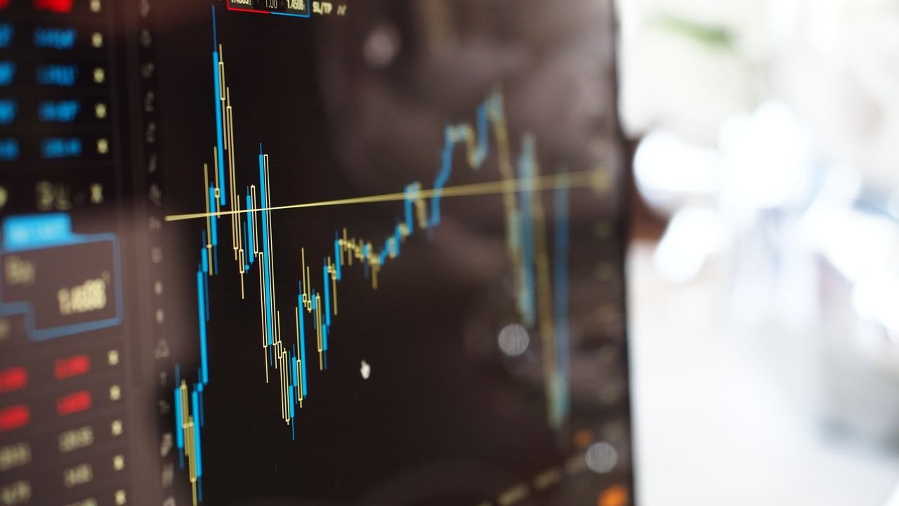Trader at a desk looking at candlestick charts on two monitors in a dim office