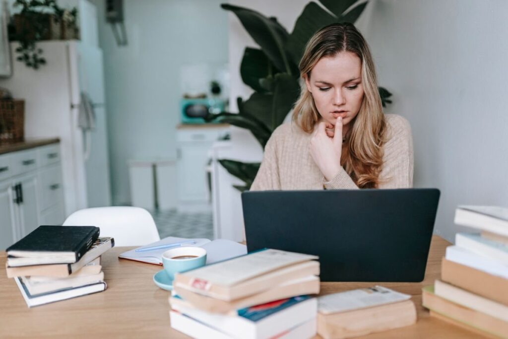Woman studying at a laptop at a kitchen table surrounded by books