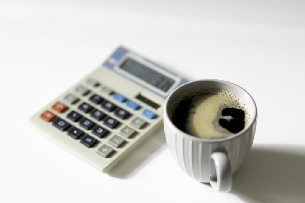 Desk calculator beside a cup of coffee, used to work out trading journal results in units of risk