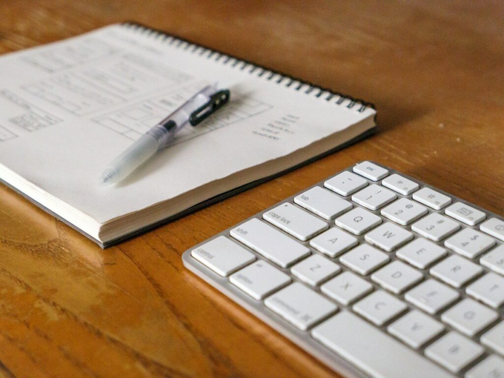 Notebook and pen beside a keyboard on a wooden desk
