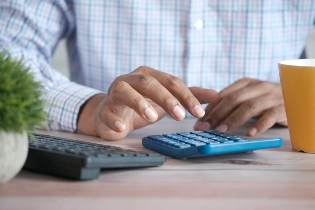 Hands using a calculator beside a keyboard, adding up what the spread costs over a month of trades