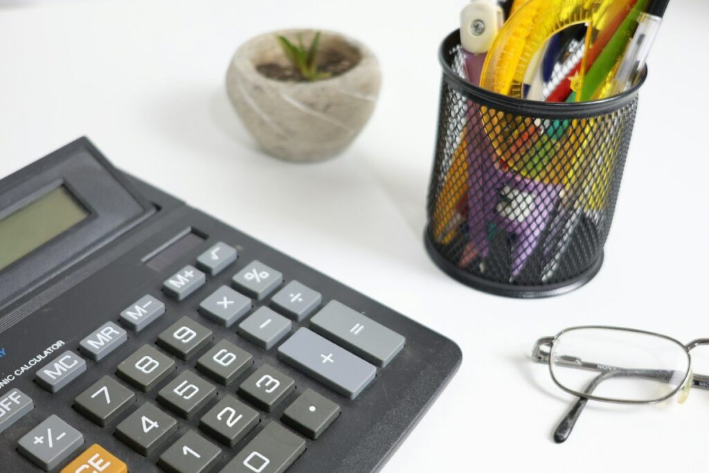 Calculator beside a pot of pens and a pair of glasses