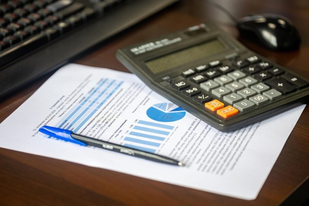 Calculator and pen on a printed report beside a keyboard