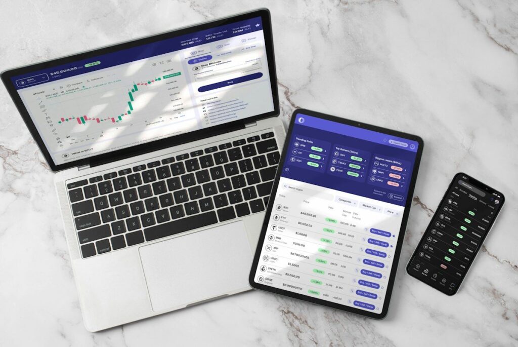 Laptop, tablet and phone showing a trading platform on a marble desk