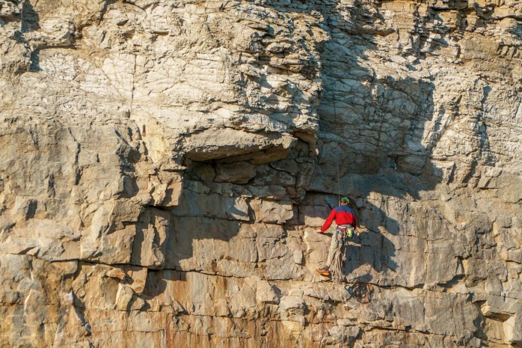 Climber in a red top on a tall rock face, like defining a ruin level before trading