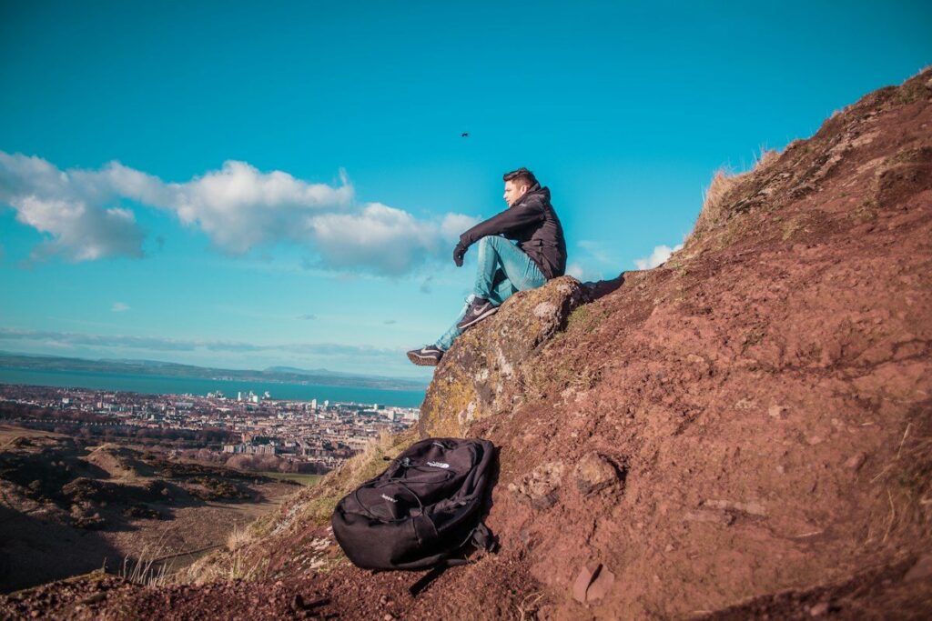 Person sitting on a rocky hillside above a town, like the pause in a flag before the trend resumes