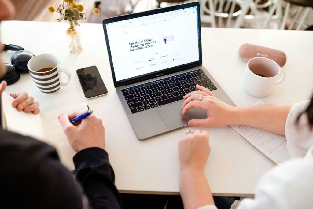 Two colleagues at a cafe table with a laptop, talking through the entry, stop and target of a range trade