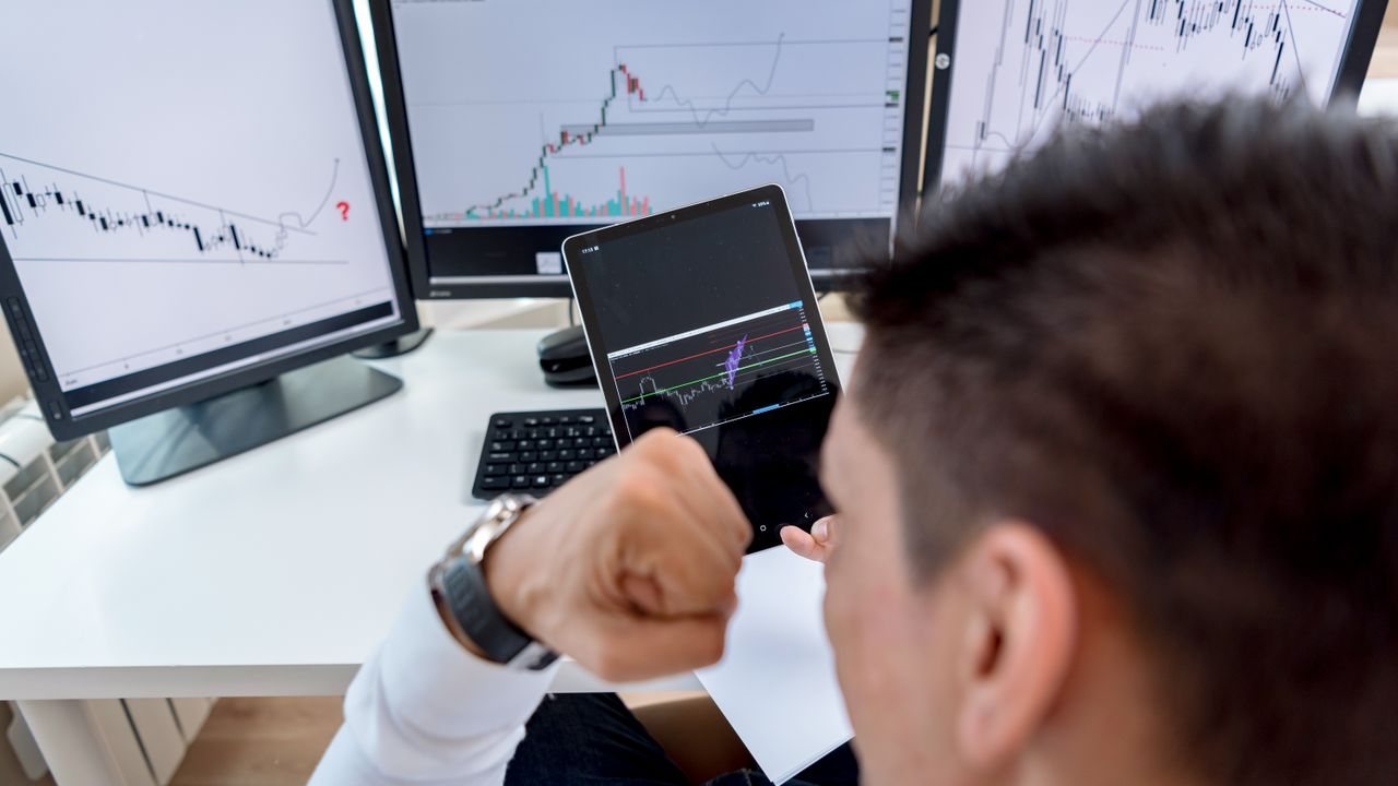 Trader with a phone in front of monitors showing stock charts
