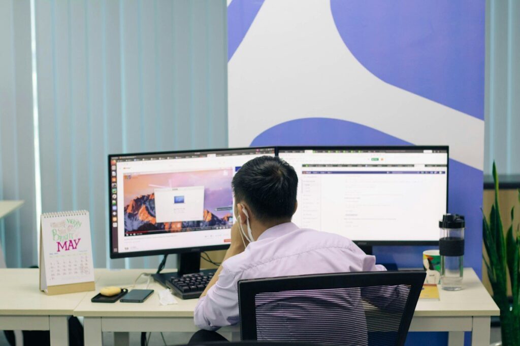 Man at a desk with two monitors in a bright office