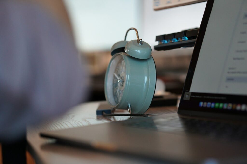 Small alarm clock beside a laptop, set for the US data release that moves gold in UK time