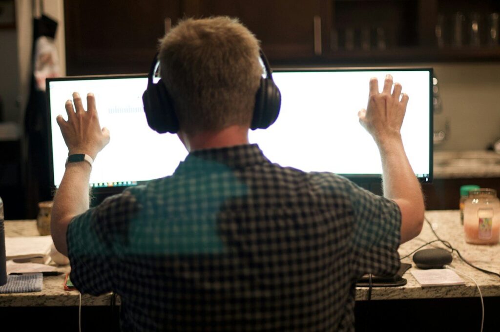 Man in headphones with his hands raised at a large monitor