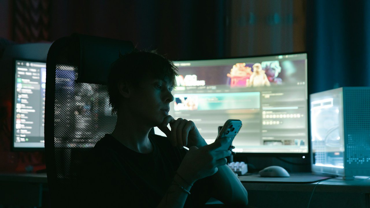 Trader on a phone in a dark room lit by large monitors