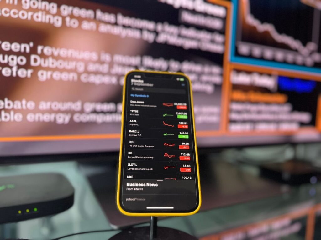 Phone showing share prices in front of a news screen