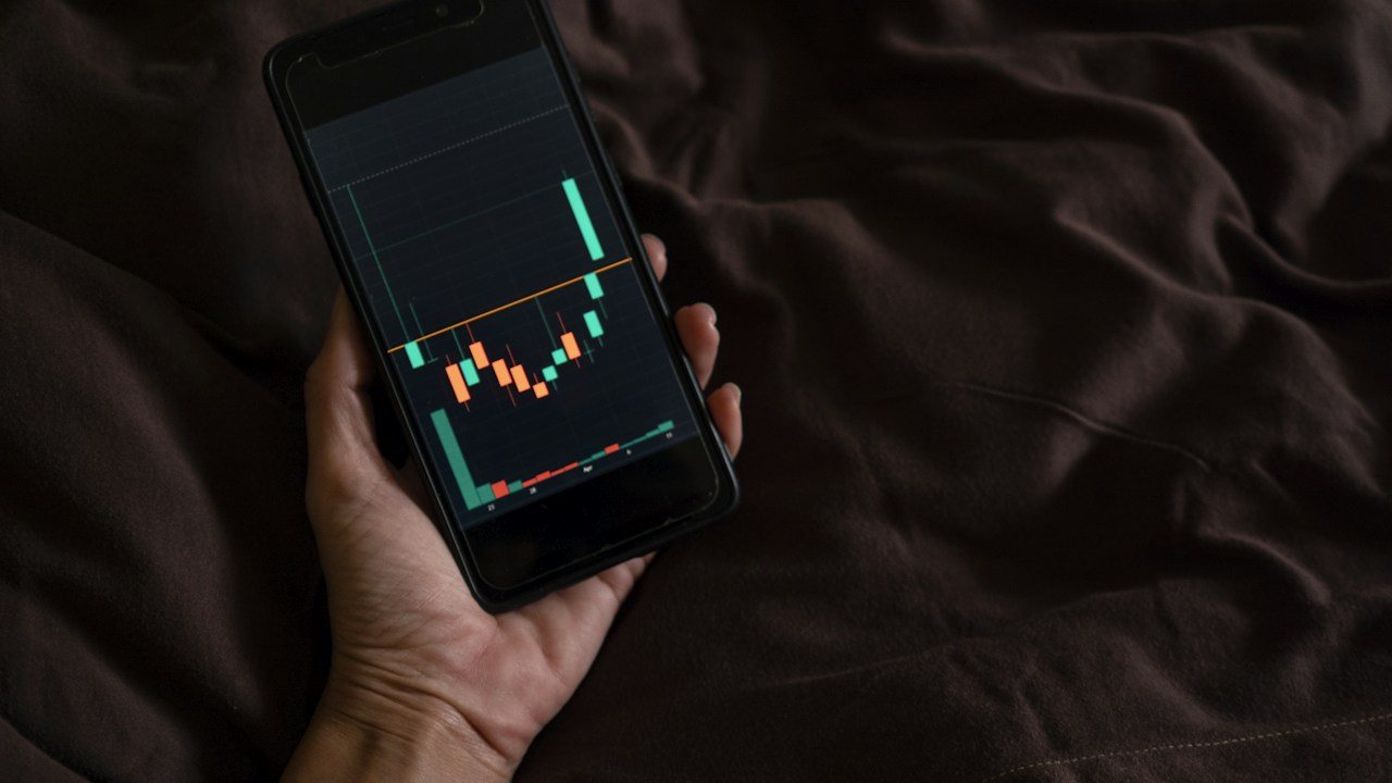 Hand holding a phone with a candlestick chart against a dark background