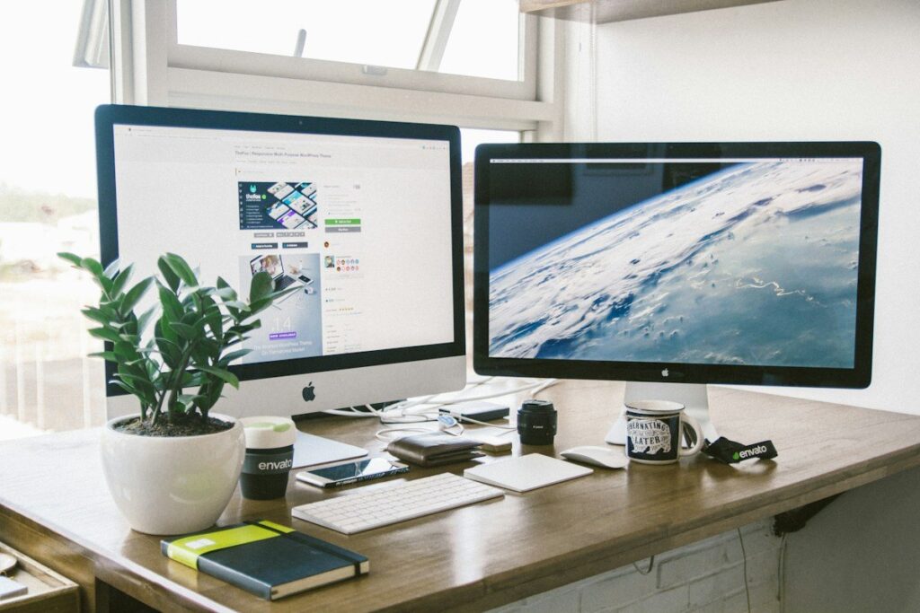 Two monitors on a desk by a window
