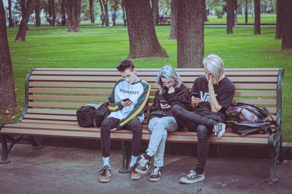 Friends looking at phones on a bench, the kind of social comparison that feeds FOMO in trading