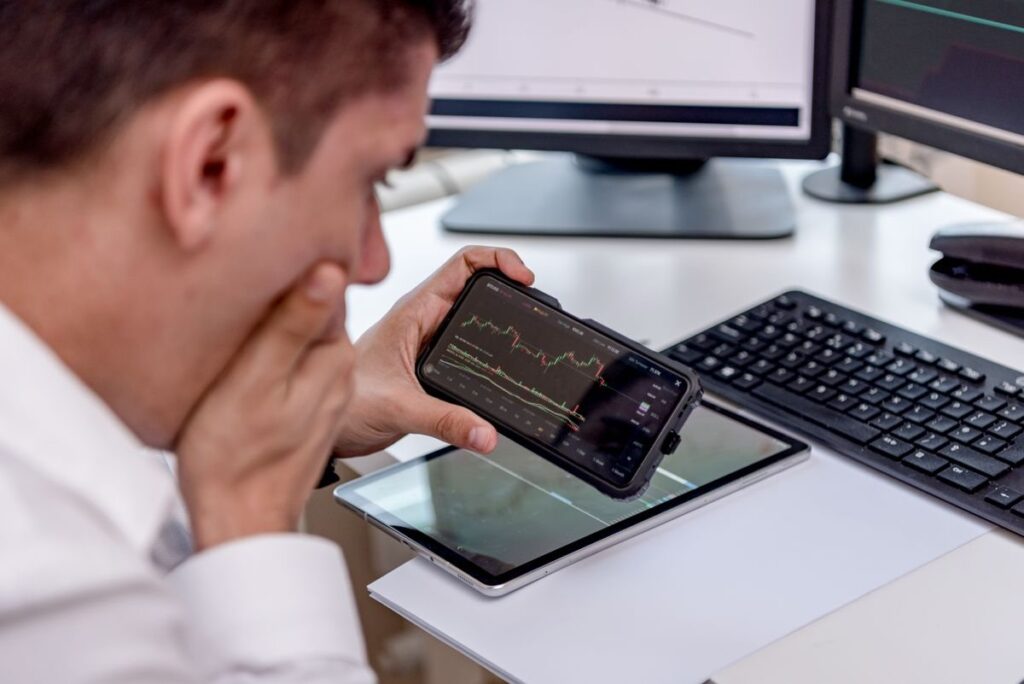 Man holding a phone with a chart in front of monitors