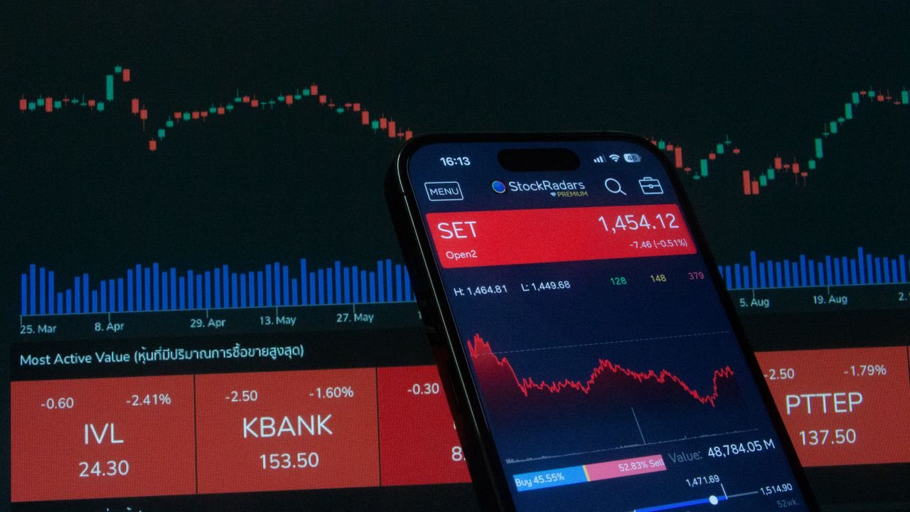Phone showing a stock trading app in front of a screen with an index chart and red price tiles