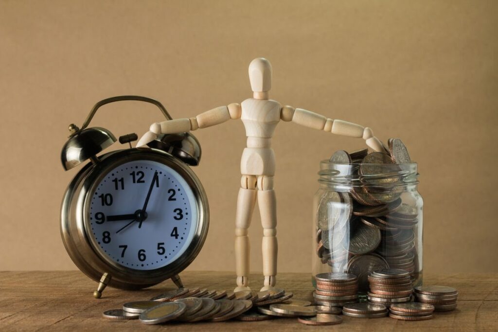 Alarm clock, wooden figure and a jar of coins on a table, like an account halved by a long run of losing trades