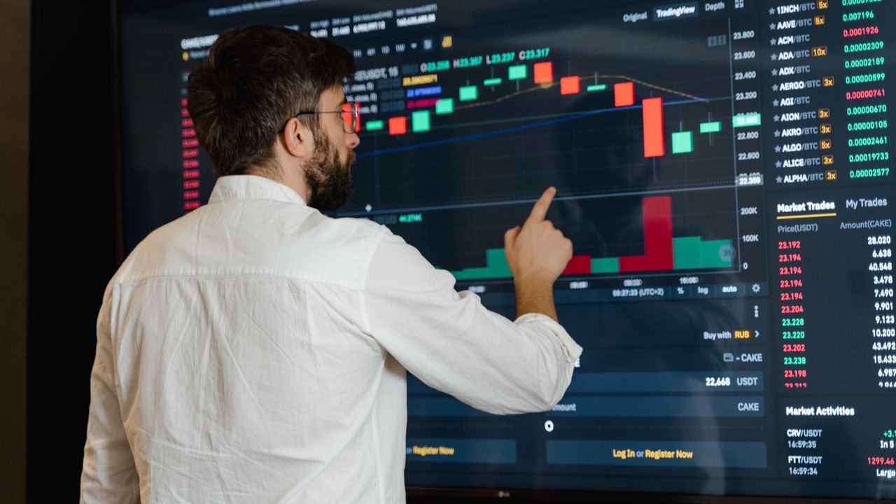 Trader pointing at a single candlestick on a monitor in a dimly lit trading room