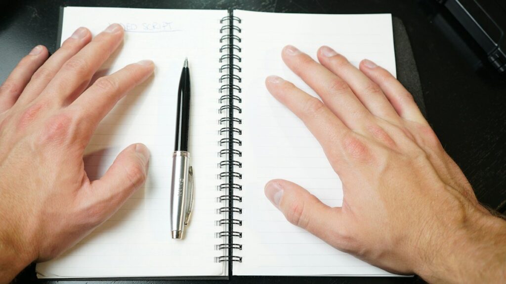 Hands resting on an open notebook with a pen, ready to mark the neckline of a double top pattern