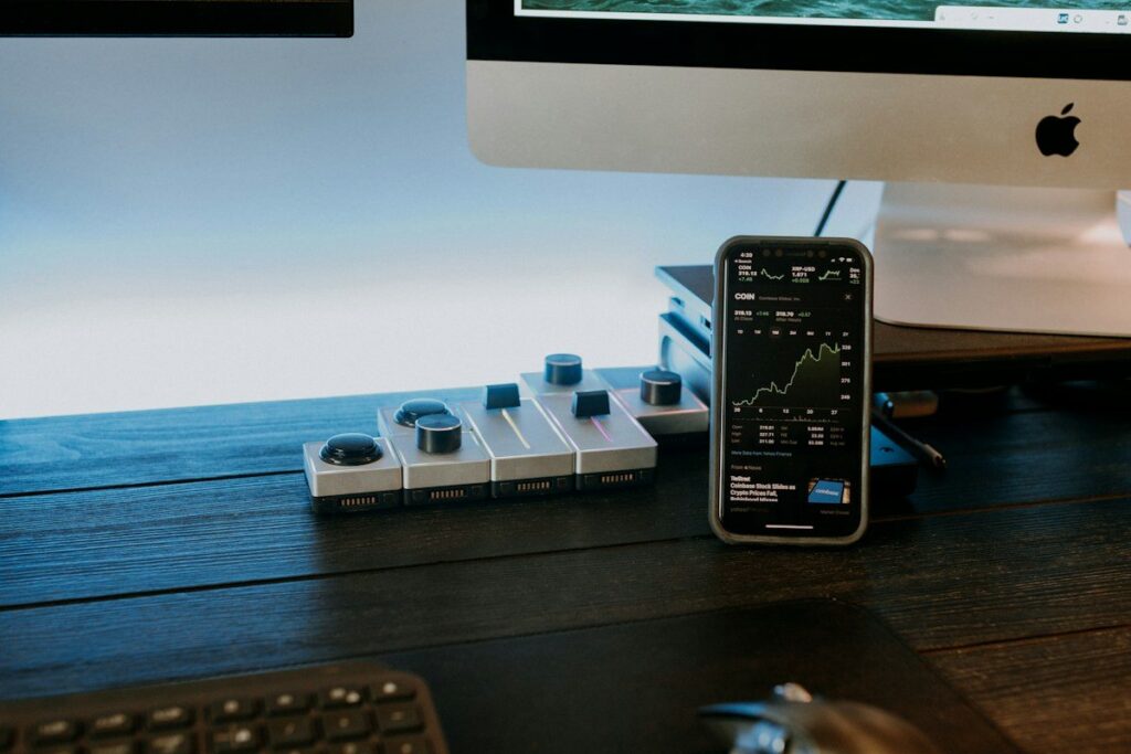 Phone showing a stock chart on a desk beside a keyboard and monitor