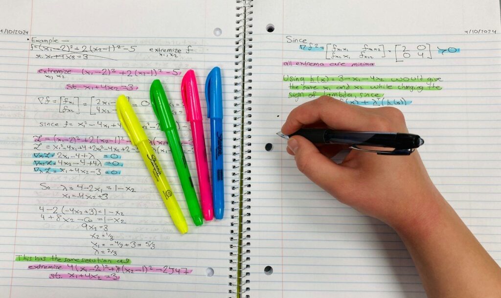 Hand writing sums in a spiral notebook, working out a spread bet stake in pounds per point