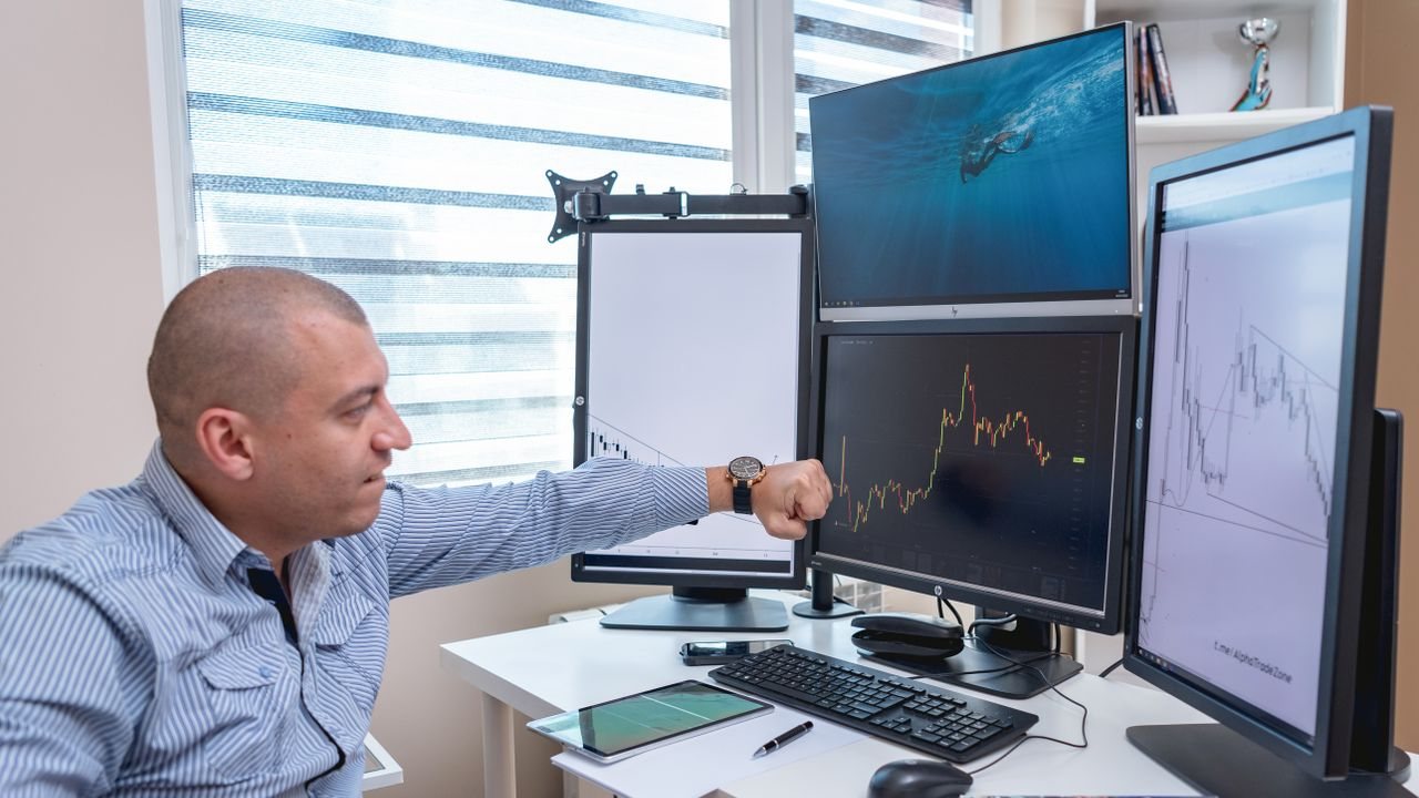 Man pointing at a monitor showing a chart at his desk
