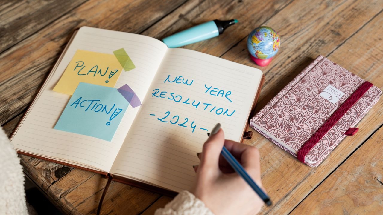 Person writing goals in a diary at a kitchen table while planning how long it takes to learn trading