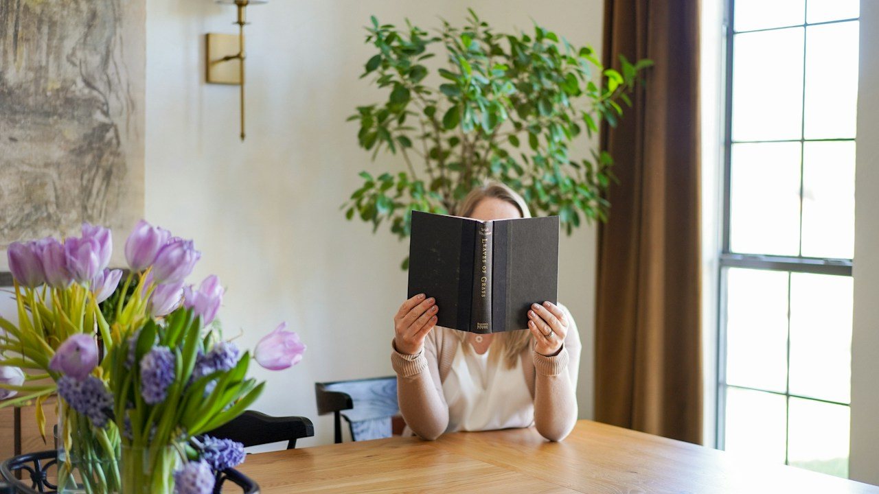 Person reading a book at a kitchen table while deciding how to choose a trading course
