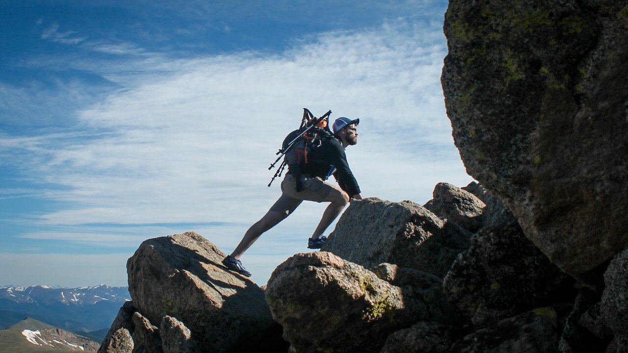 Hiker climbing rocks near a summit, like a trade approaching its planned take-profit target