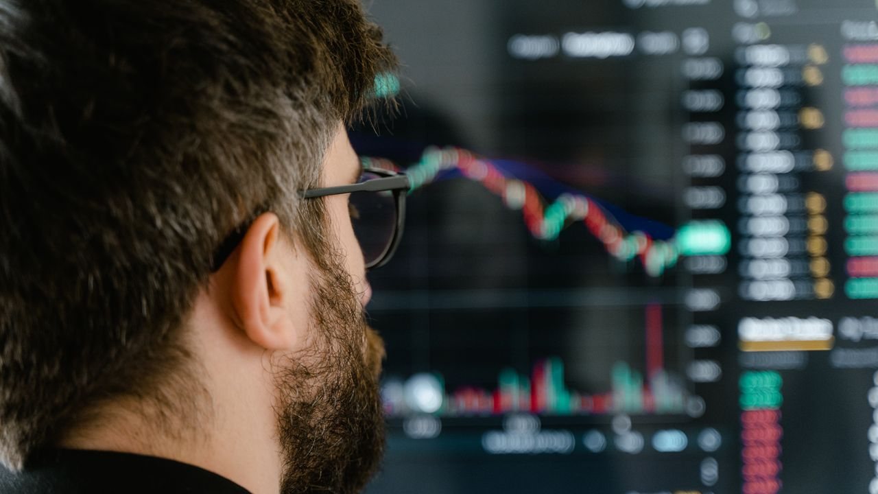 Trader at a desk studying a price chart with a momentum indicator panel on two monitors