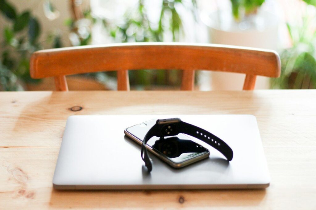 Closed laptop with a smartphone and watch on a wooden table, the start of a beginner's trading roadmap