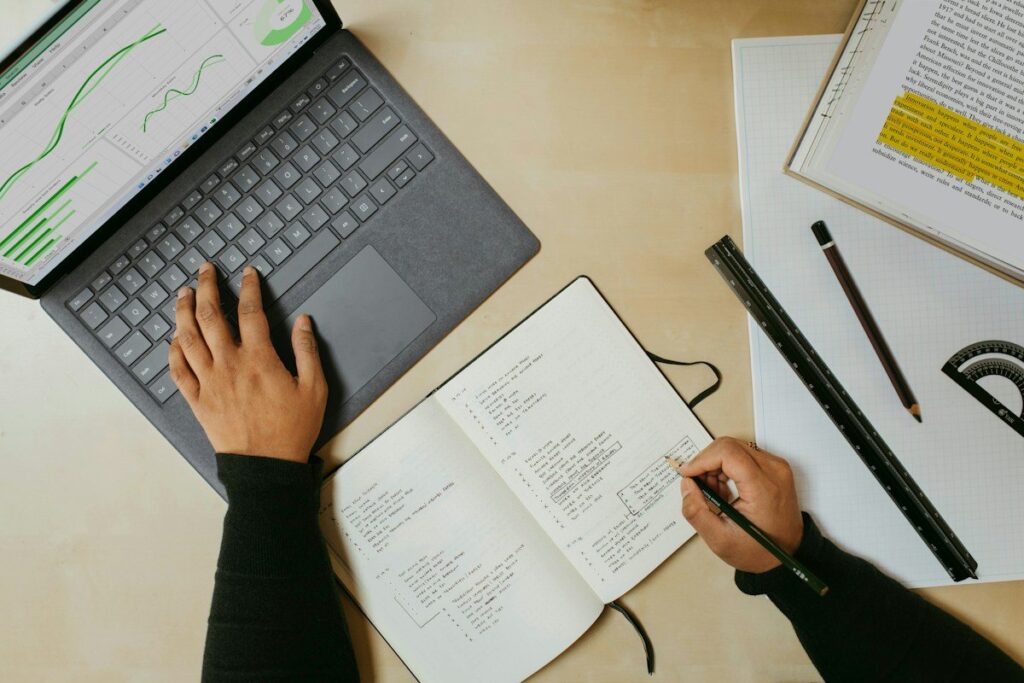 Notebook with a handwritten pattern checklist beside a monitor showing trading charts