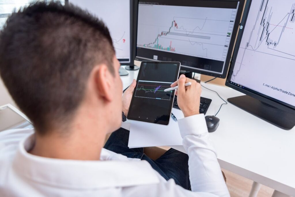 Man drawing on a tablet in front of chart monitors