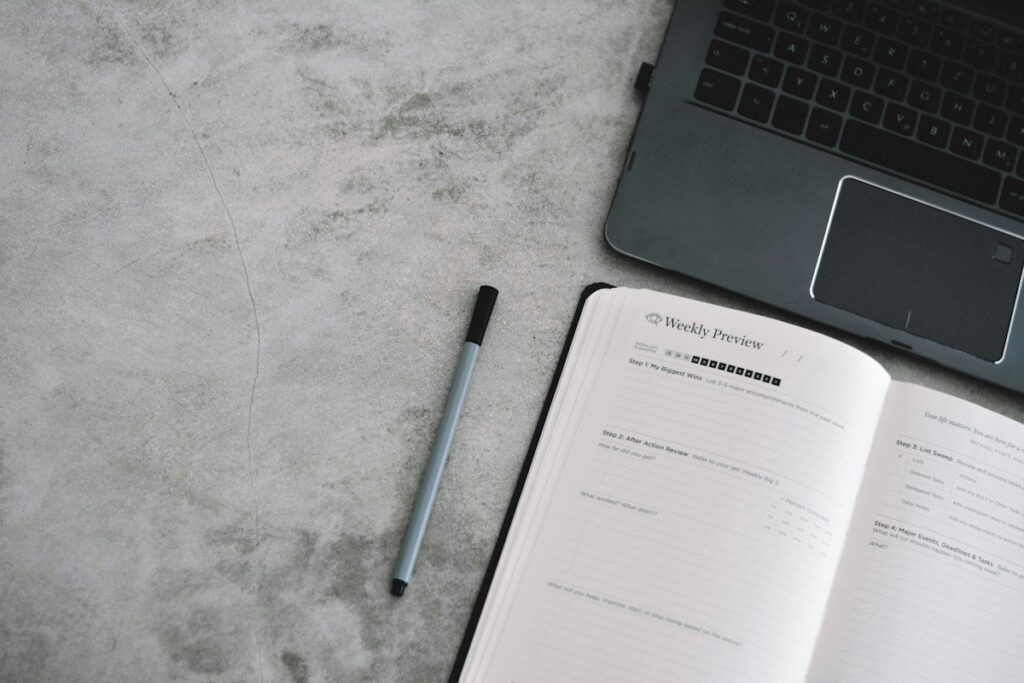 Open notebook and pen beside a laptop