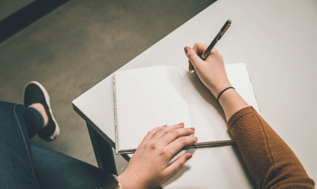 Hand writing in an open notebook, reviewing each losing trade to find the cause of a drawdown