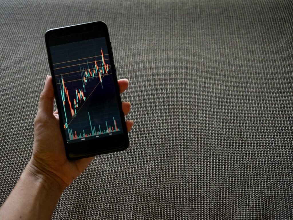 Hand placing a stop order on a smartphone trading app just beyond a price ceiling
