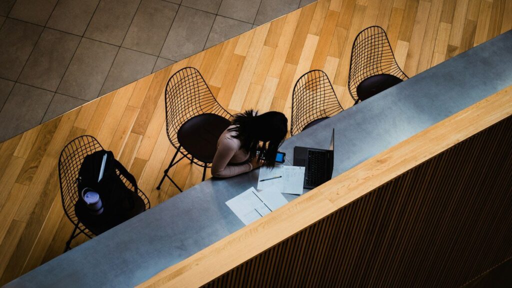 Person at a counter with a laptop and printed papers, seen from above, checking real trade results rather than memory