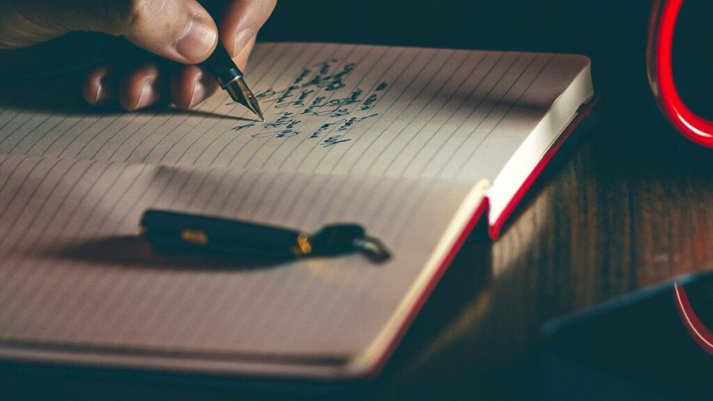 Hands writing a list of questions in a notebook before choosing a trading course