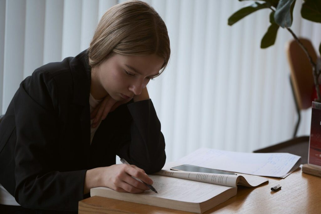 Person writing in a ledger book at a desk, recording a tax year's results from CFDs and spread bets