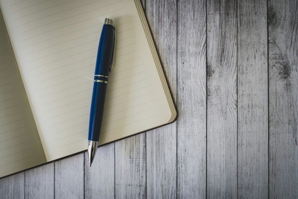 Open notebook and a blue pen on a grey wooden table, ready to note a fixed set of timeframes