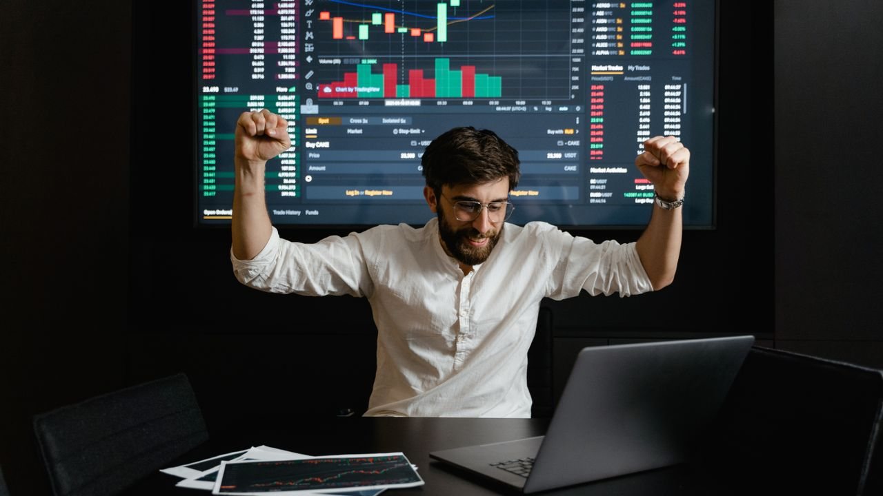 Trader celebrating at a desk in front of a wall of charts