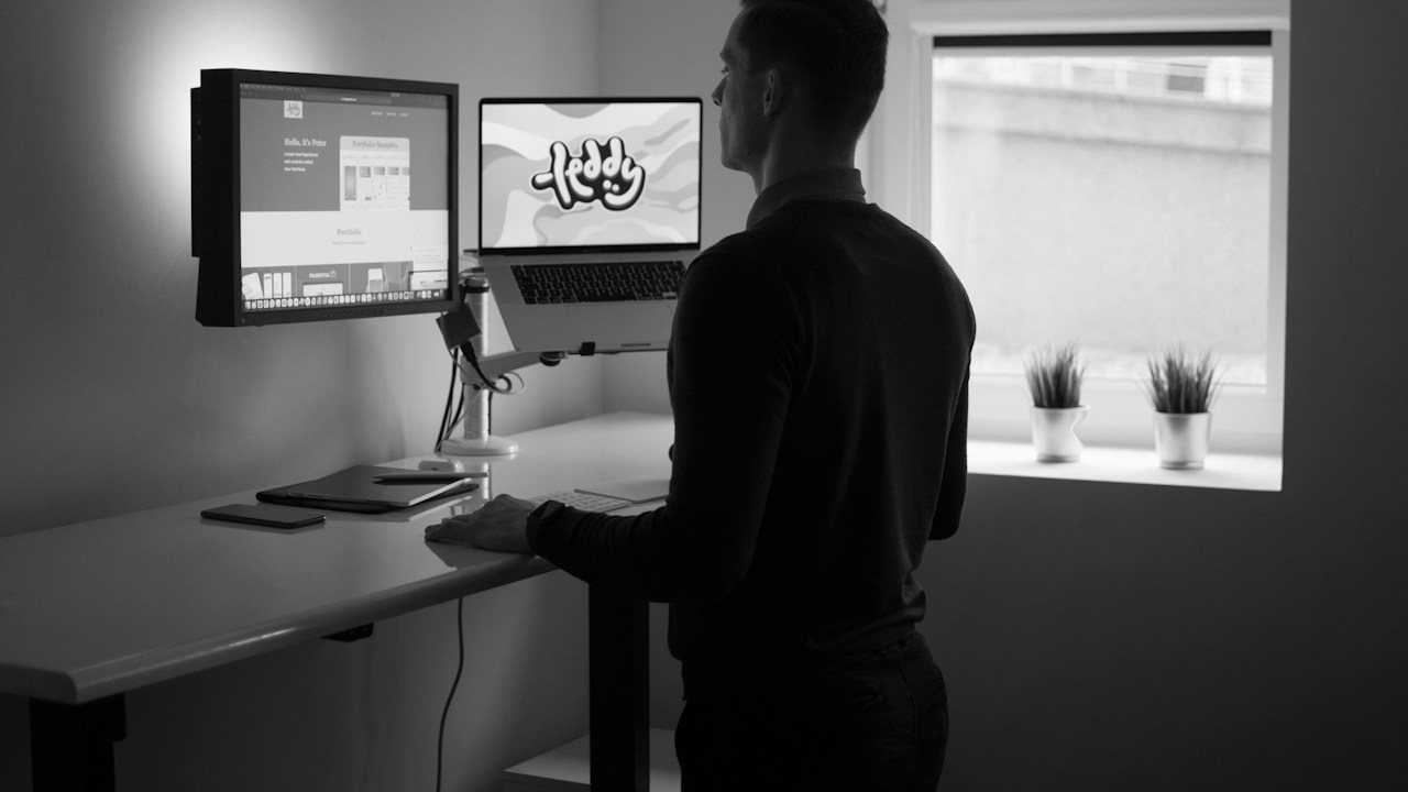 Trader at a standing desk comparing price action vs indicators on two screens