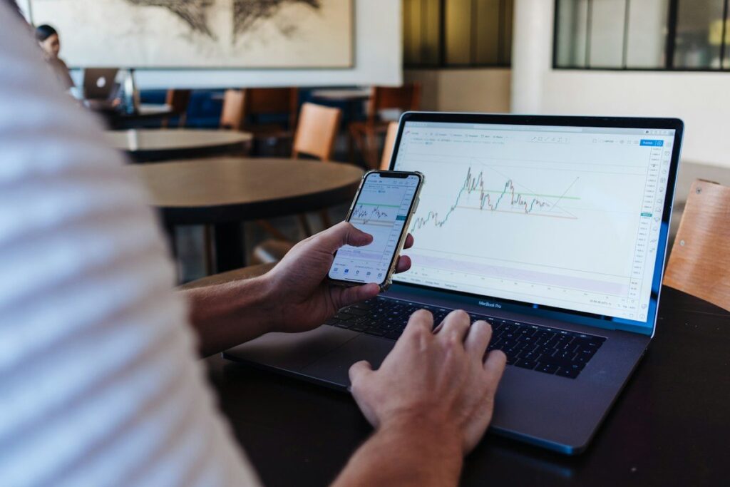 Hands with a phone and a laptop showing a line chart