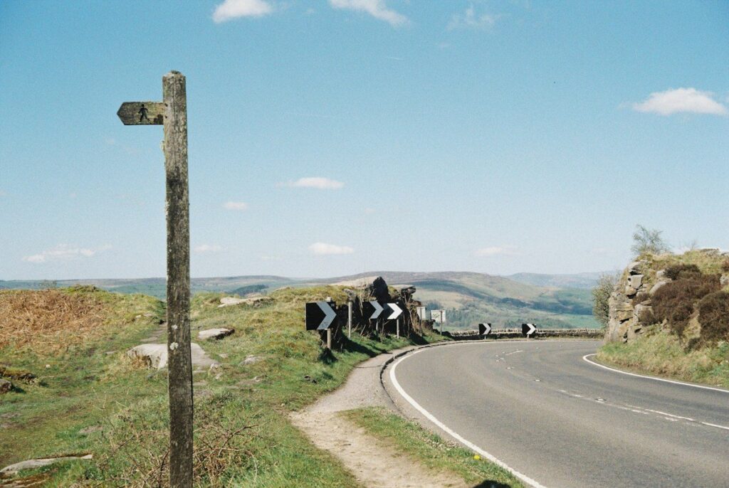 Wooden signpost pointing two ways on a country lane, a choice between spread betting and CFDs