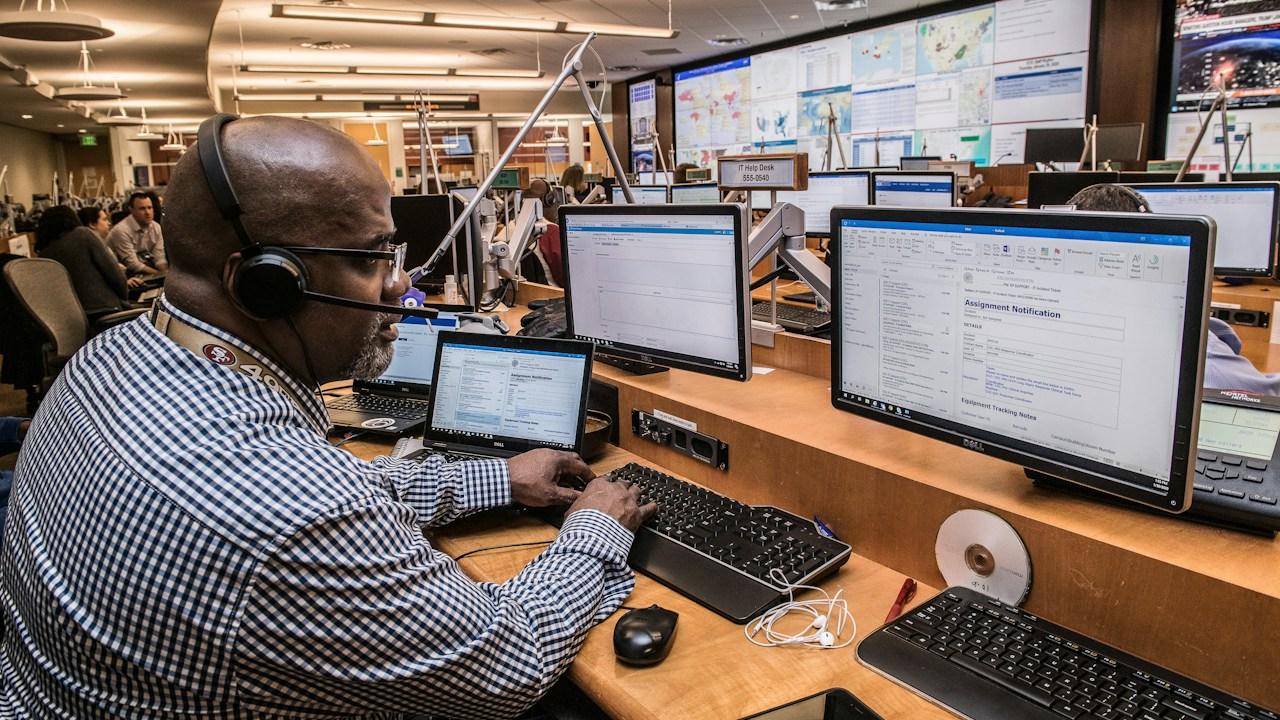 Operator at a desk with many monitors in a busy control room
