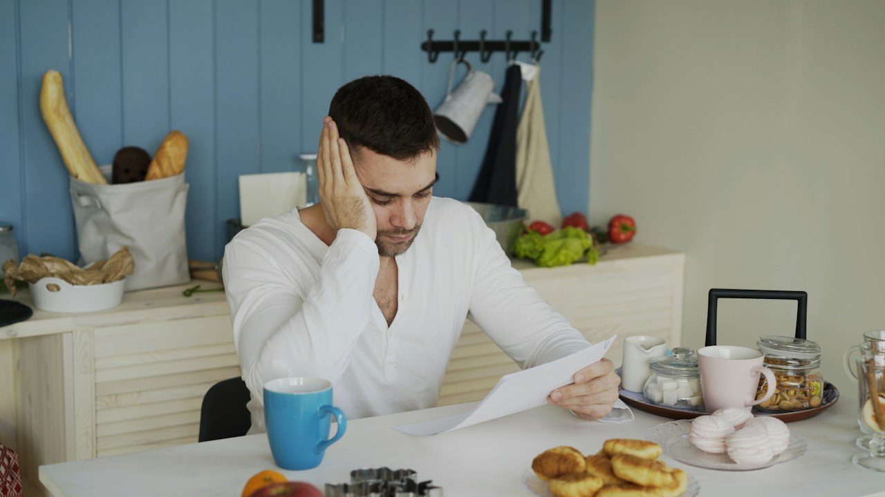 Man reading a letter at a kitchen table, learning what spread betting is before opening an account